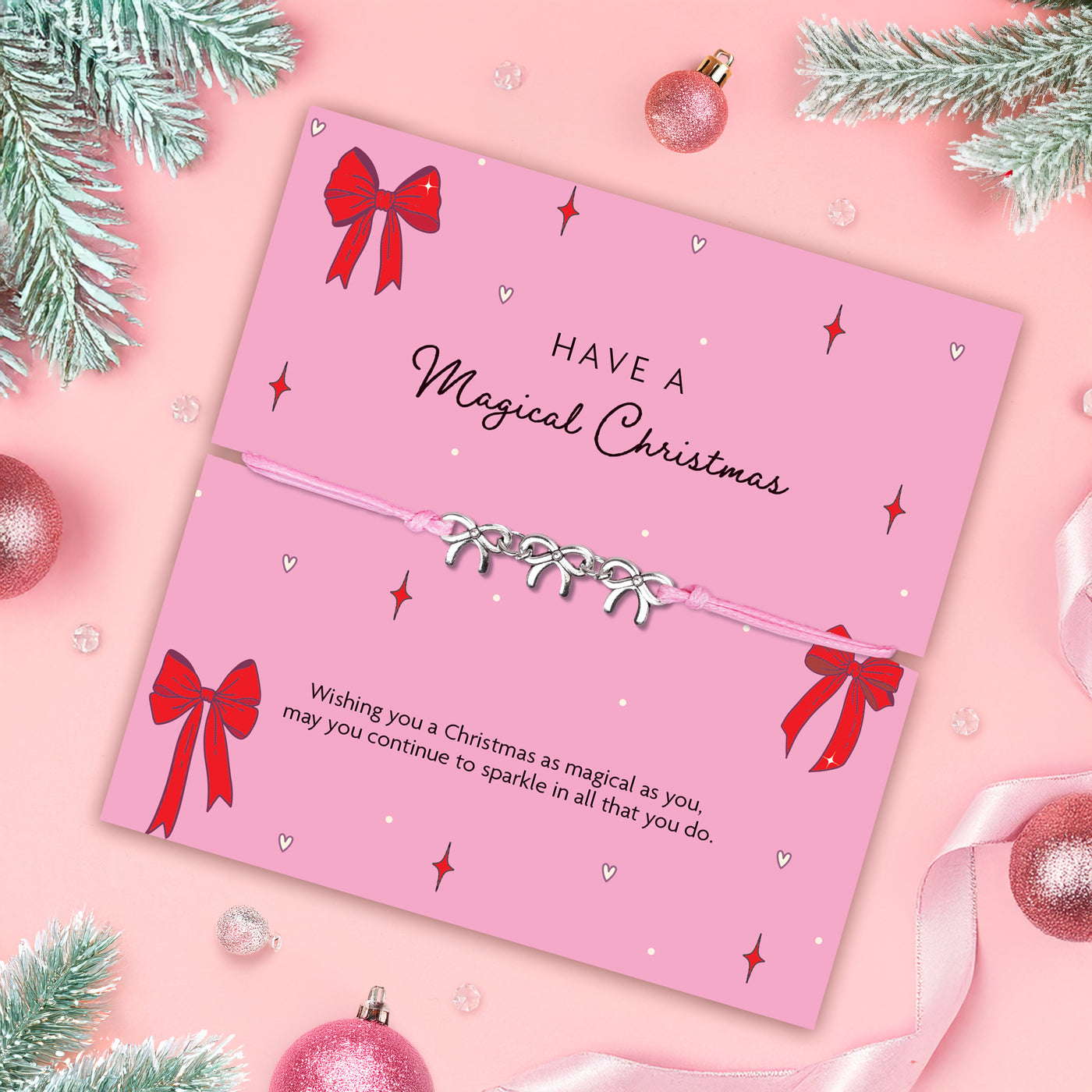 Pink Christmas card with red bows and decorative text on a pink background with a friendship bracelet with bow charms. A meaningful gift under £10 for Christmas.