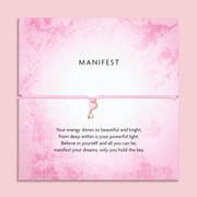 Pink 'Manifest' bracelet with heart key charm on a soft pink poem card with a motivational message. A motivational gift for a friend. 