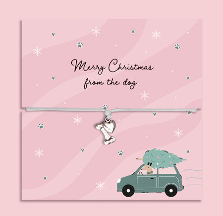 Merry Christmas from the Dog bracelet featuring a silver plated bone and heart charm on an adjustable cord, presented on a festive pink card with paw prints, snowflakes, and a dog carrying a Christmas tree illustration. Includes a soft pouch for gifting and safekeeping. Perfect Christmas jewellery gift from the dog to their owner, stocking filler for pet lovers, or sentimental festive bracelet for dog mums and dads to celebrate the bond with their furry friend.