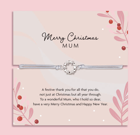 Merry Christmas Mum bracelet featuring a silver wreath charm on an adjustable cord, presented on a festive pink card with berries, leaves, and snowy details. Includes a soft white pouch for gifting and safekeeping. A sentimental Christmas jewellery gift for mum, perfect as a stocking filler, Christmas morning surprise, or meaningful keepsake to show love and appreciation during the festive season.