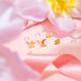 Gold-plated stainless steel star and crescent moon stud earrings with butterfly backs, styled on a soft pink background with floral accents and ribbon.