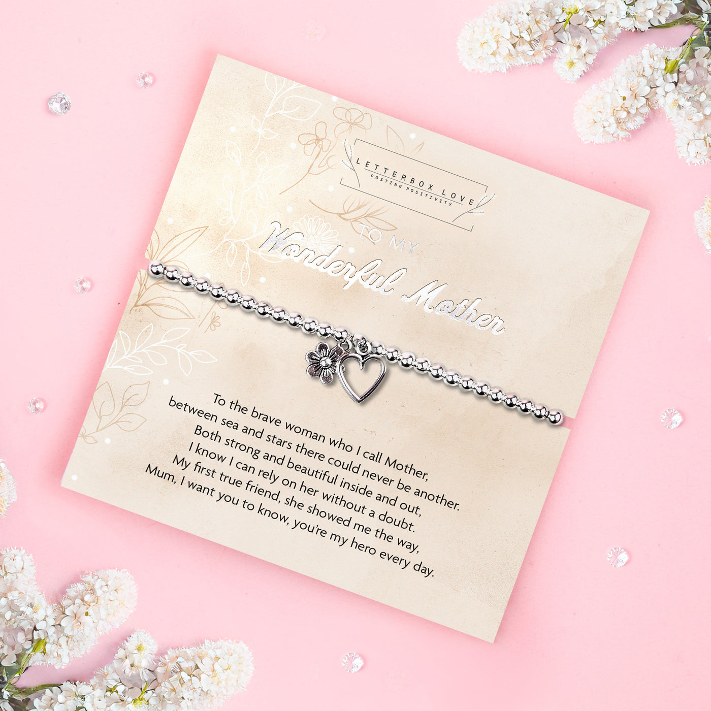 A silver beaded bracelet with a heart and flower charm displayed on a card reading 