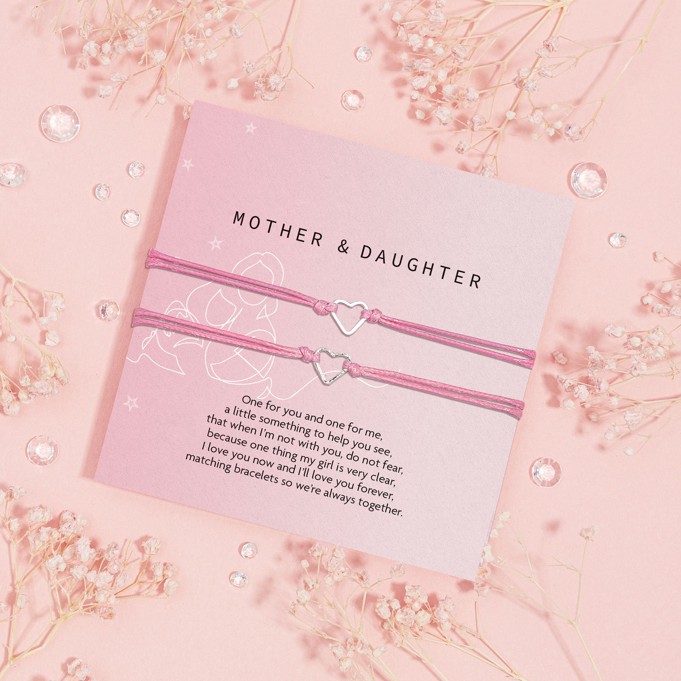Pair of pink corded bracelets with heart-shaped charms presented on a lavender 'MOTHER & DAUGHTER' card, with a touching message about love and togetherness, adorned with baby's breath flowers and crystal accents on a pastel pink backdrop.