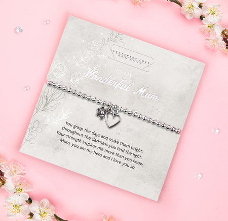 A silver beaded bracelet with a heart and flower charm displayed on a card reading 