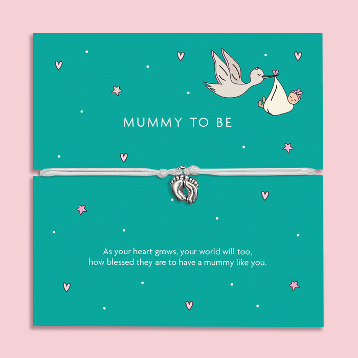 A turquoise card with the words "MUMMY TO BE" in white uppercase letters. The card is decorated with soft pink hearts, stars, and an illustration of a stork carrying a baby wrapped in a bundle. A delicate silver baby feet charm bracelet on a soft ivory cord is wrapped around the card. Below, the message reads: "As your heart grows, your world will too, how blessed they are to have a mummy like you." 