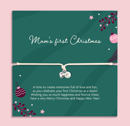 A square poem card with a thin white bracelet across the center and small heart and pearl charms. The card is dark green with white script reading 'Mum's first Christmas' and smaller white text below, decorated with Christmas ornaments, stars, and foliage on a light pink background.