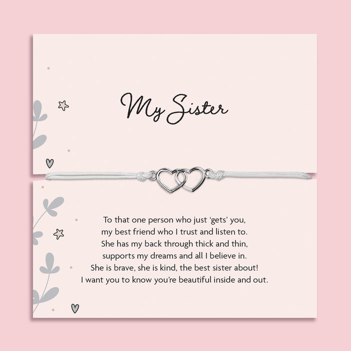 My Sister bracelet featuring two silver interlocking heart charms on an adjustable cord, presented on a blush pink card with a heartfelt message about sisterhood. Wrapped in pink tissue paper, ready for gifting. A sentimental jewellery gift for sisters, perfect for birthdays, Christmas, or just to show appreciation. A meaningful bracelet symbolising love, friendship, and connection between sisters.