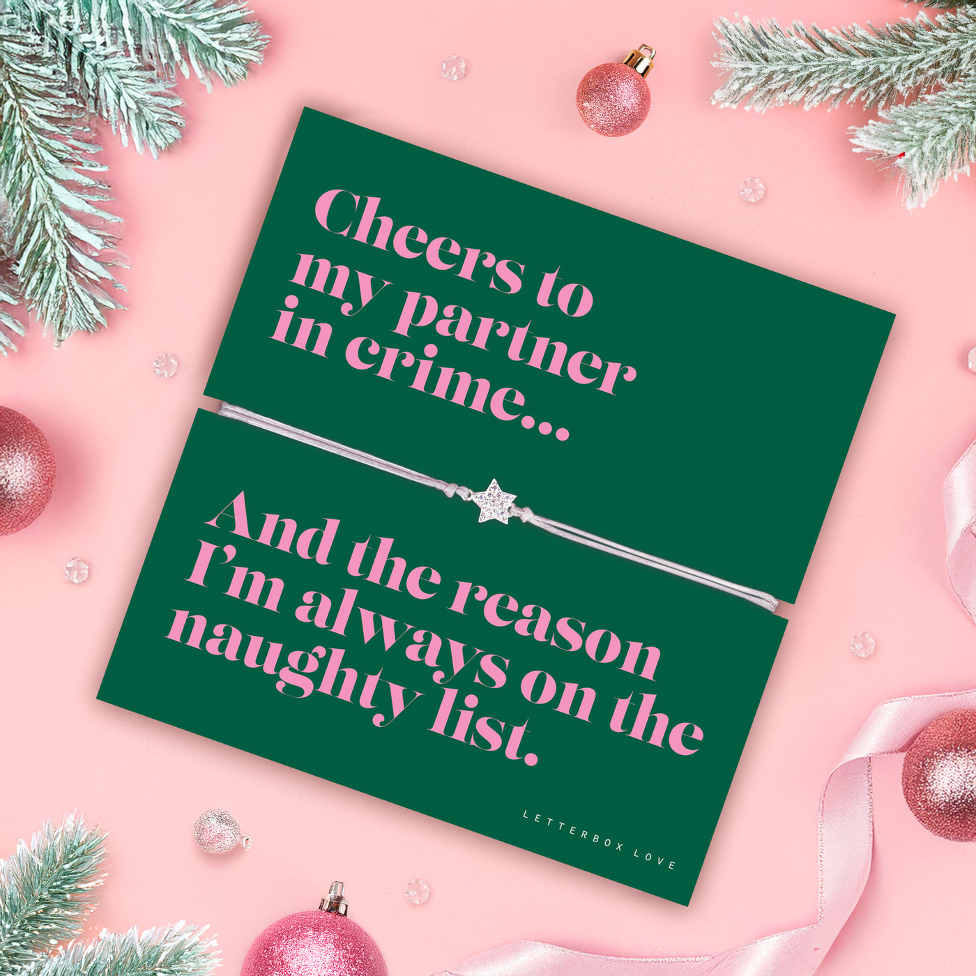 Green card with pink text and a silver bracelet on a pink background with Christmas decorations.