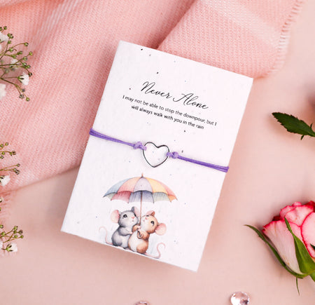 Letterbox Love Never Alone bracelet with a silver heart charm, set on a card with an illustration of two mice sharing an umbrella and a sentimental message. Thoughtful friendship gift, featuring eco-friendly seed paper design.