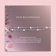 Flat lay of a “New Beginnings” bracelet gift by Letterbox Love, featuring a double silver box chain with star and bead charms, displayed on a mauve-toned sentiment card with floral illustrations and an inspiring message.