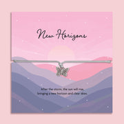 Butterfly charm bracelet on a card with 'New Horizons' text and mountain landscape design. A gift for someone on a new beginnings.