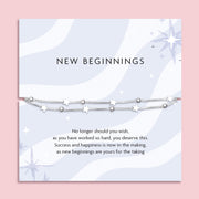 Silver star and bead bracelet displayed on a pastel backing card with the message "New Beginnings." The background features soft wavy patterns and star illustrations. Below the bracelet, a motivational poem reads: "No longer should you wish, as you have worked so hard, you deserve this. Success and happiness is now in the making, as new beginnings are yours for the taking.