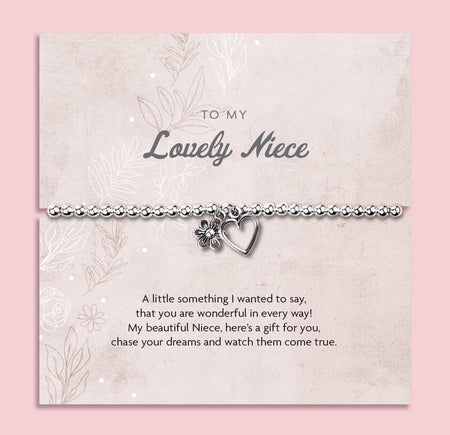 A silver beaded bracelet with a heart and flower charm displayed on a card reading 