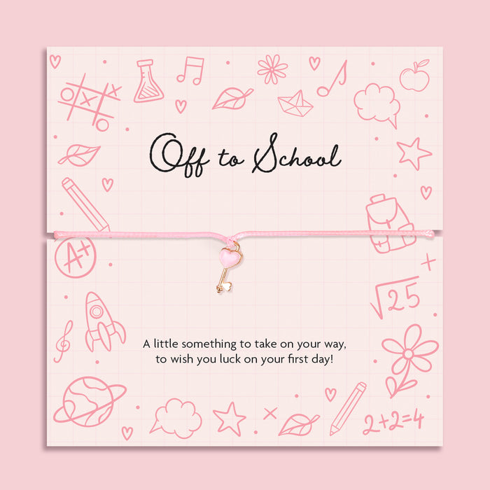 Pink cord bracelet with a rose gold heart key charm, displayed on a school-themed sentiment card reading 'Off to School ' A little something to take on your way, to wish you luck on your first day!” from Letterbox Love.