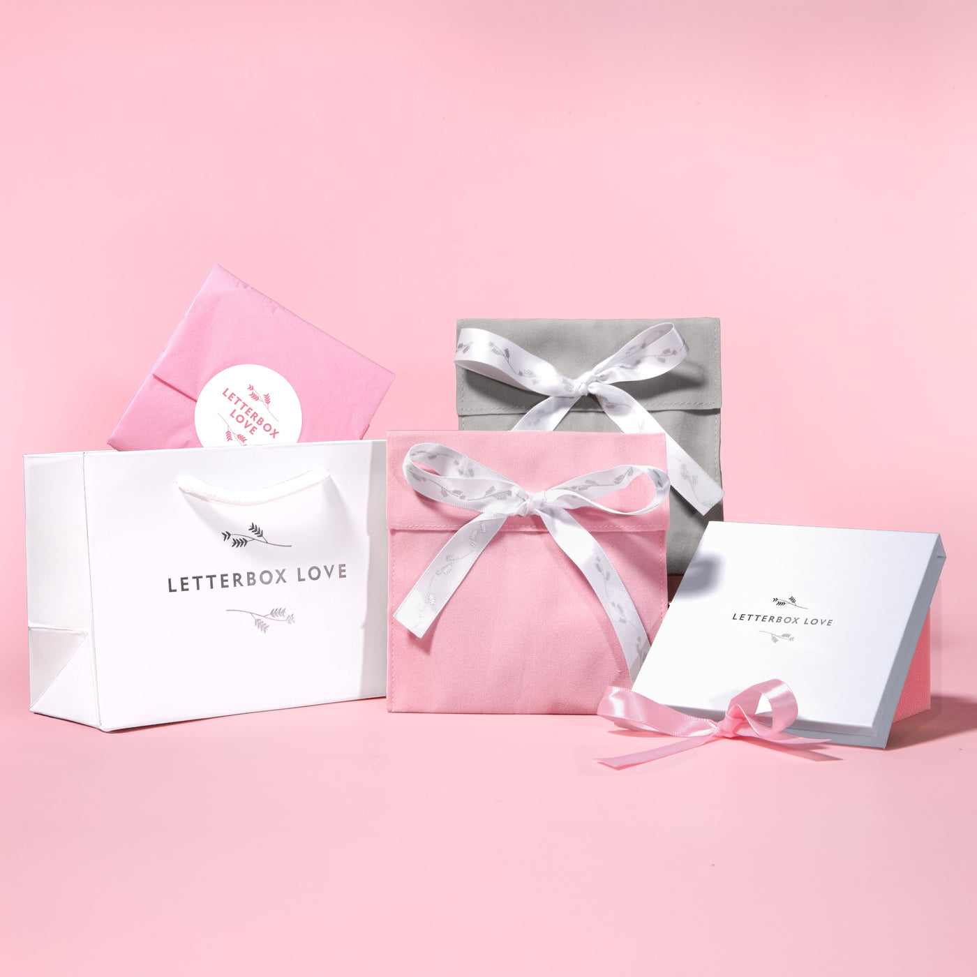 Gift boxes with ribbons and 'Letterbox Love' branding on a pink background