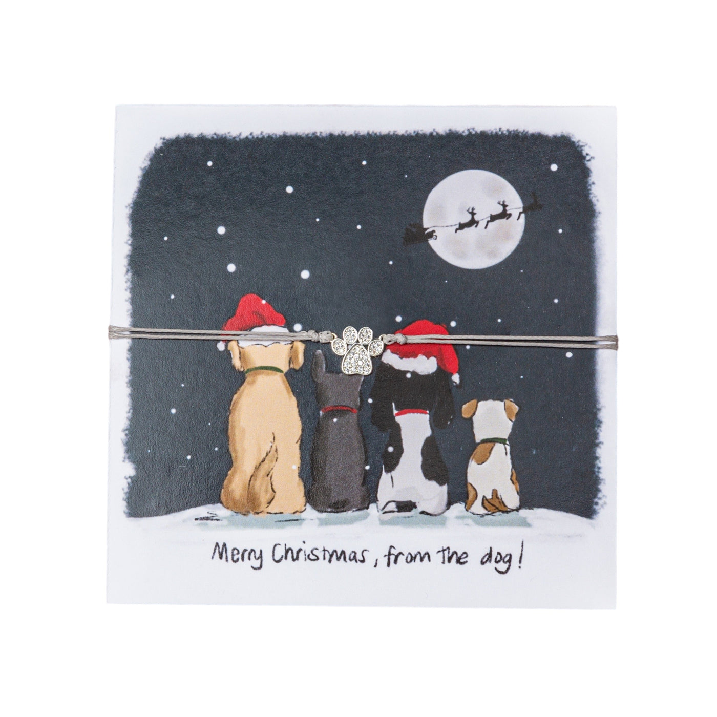 Festive greeting card featuring an illustration of four dogs in Santa hats looking up at a night sky with snowflakes, a full moon, and Santa's sleigh flying past. A paw-shaped bracelet charm with glittering stones is tied to the card with a string, enhancing the festive appearance. Below the scene is the humorous phrase 'Merry Christmas, from the dog!' 