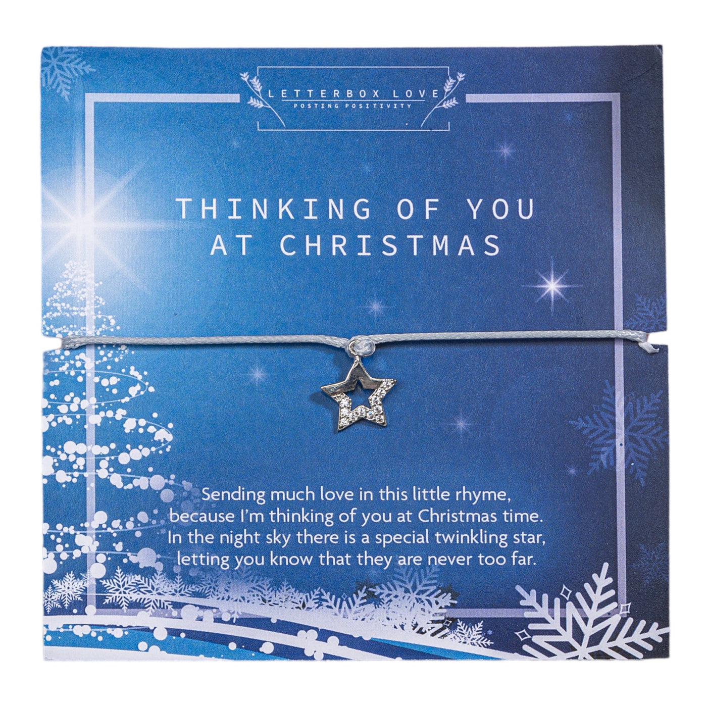 A festive Christmas card with a deep blue and white color scheme, featuring the message 'THINKING OF YOU AT CHRISTMAS' in elegant, capitalized white letters. The design includes sparkling stars, snowflakes, and an abstract Christmas tree, creating a wintry night sky effect. A star-shaped pendant with a glittering stone in the center is tied to the front of the card, adding a touch of sparkle. 