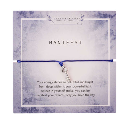 A “Manifest” wish bracelet featuring a silver key charm on a blue cord, centered on a marbled gray and white card with an inspirational quote encouraging self-belief and the manifestation of dreams.