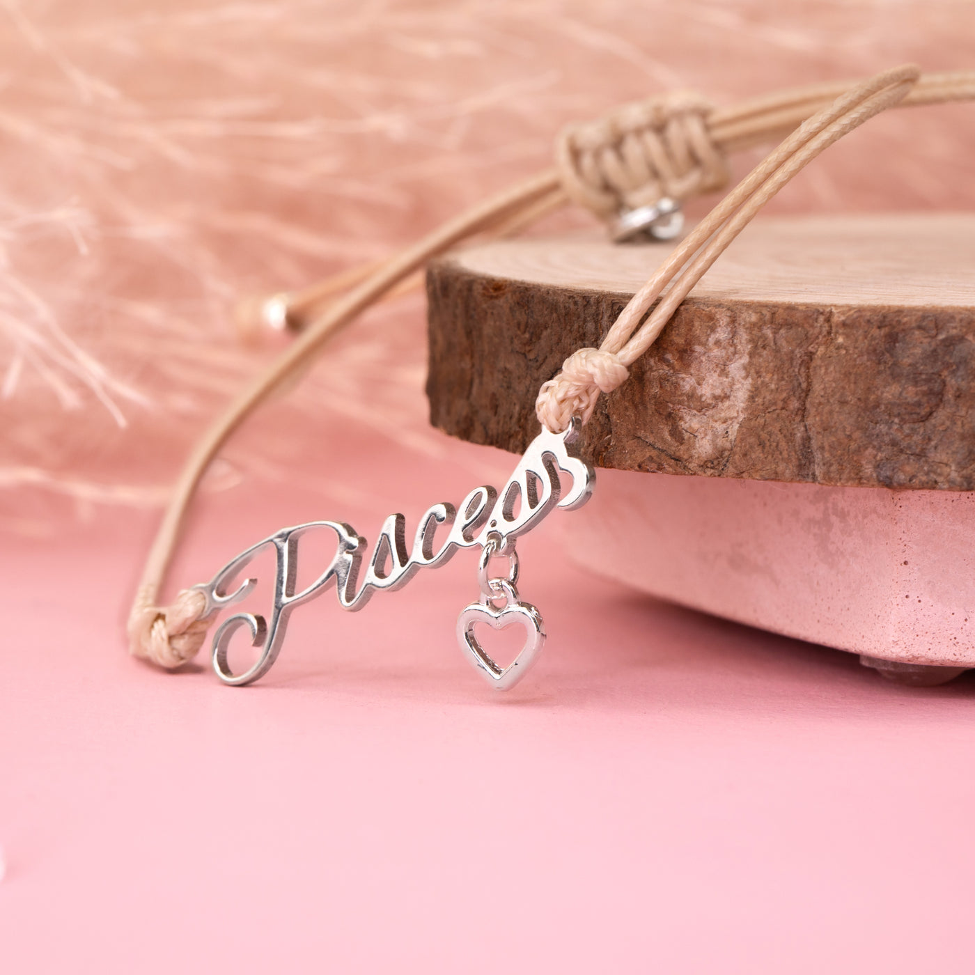 Silver 'Pisces' charm with a heart on a beige cord against a pink background. Jewellery under £20 for her. Pisces bracelet for a friend