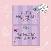 A silver beaded bracelet with a heart charm and bow pendant displayed on a lavender card that reads 'A LITTLE SOMETHING JUST TO SAY.