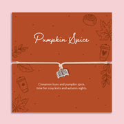 Neutral adjustable cord bracelet with silver-tone open book charm displayed on a rust Pumpkin Spice autumn card with leaves, coffee cup and cinnamon bun illustrations.
