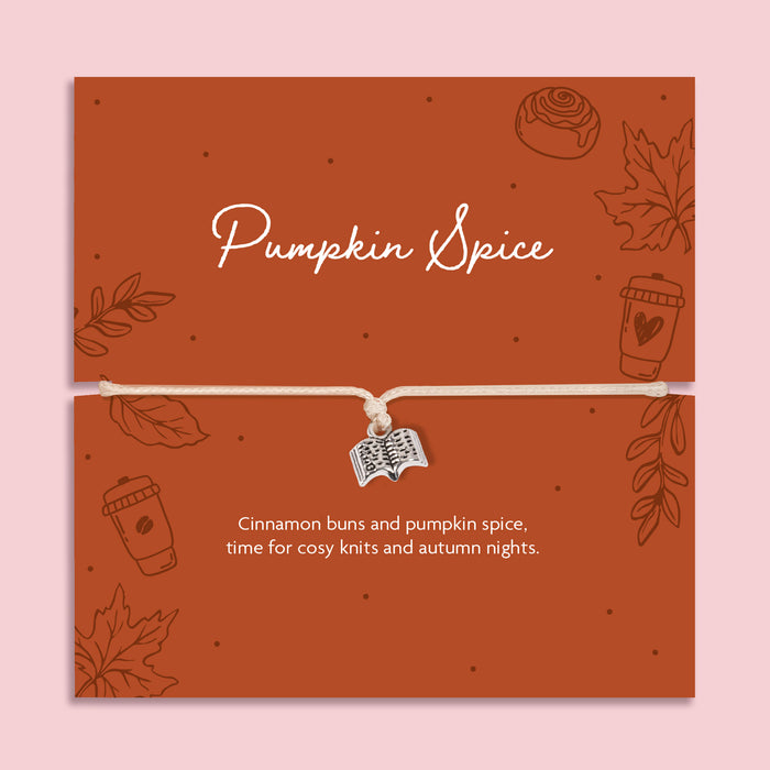 Neutral adjustable cord bracelet with silver-tone open book charm displayed on a rust Pumpkin Spice autumn card with leaves, coffee cup and cinnamon bun illustrations.