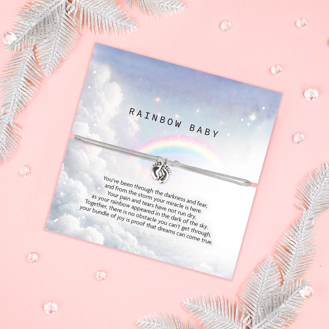 An image of a sentimental card featuring a silver bracelet with a small charm of intertwined hands. The card has a soft, dreamy design with a cloudy sky and a rainbow in the background. The text on the card reads 