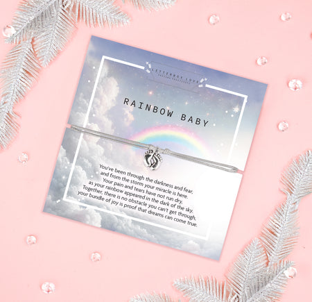 An image of a sentimental card featuring a silver bracelet with a small charm of intertwined hands. The card has a soft, dreamy design with a cloudy sky and a rainbow in the background. The text on the card reads 