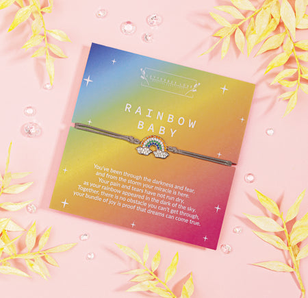 Vibrant card titled 'RAINBOW BABY' featuring a touching message about hope and miracles, accompanied by a delicate bracelet with a sparkling rainbow charm. The card, with gradient hues of a sunset.