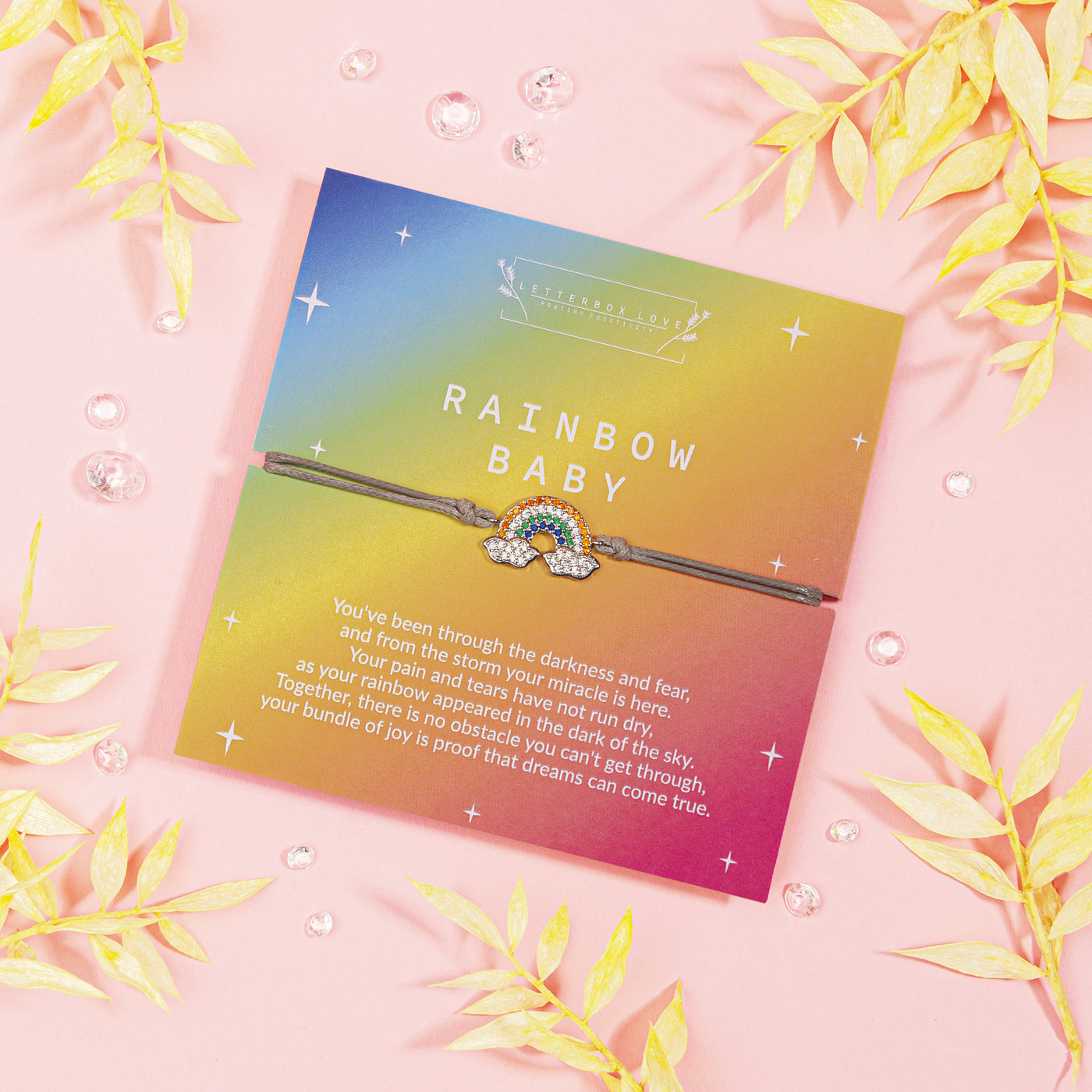 Vibrant card titled 'RAINBOW BABY' featuring a touching message about hope and miracles, accompanied by a delicate bracelet with a sparkling rainbow charm. The card, with gradient hues of a sunset.