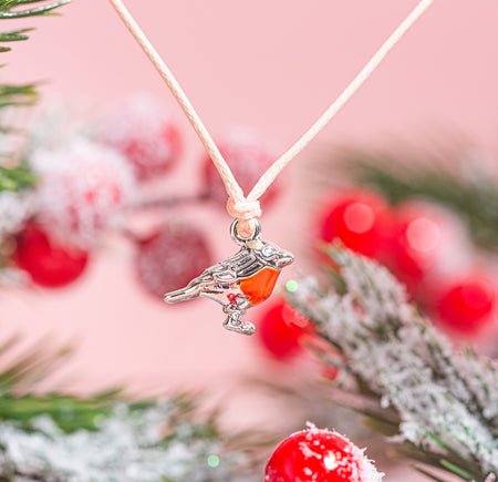 Necklace with a bird and berry pendant against a festive background with red berries and greenery.