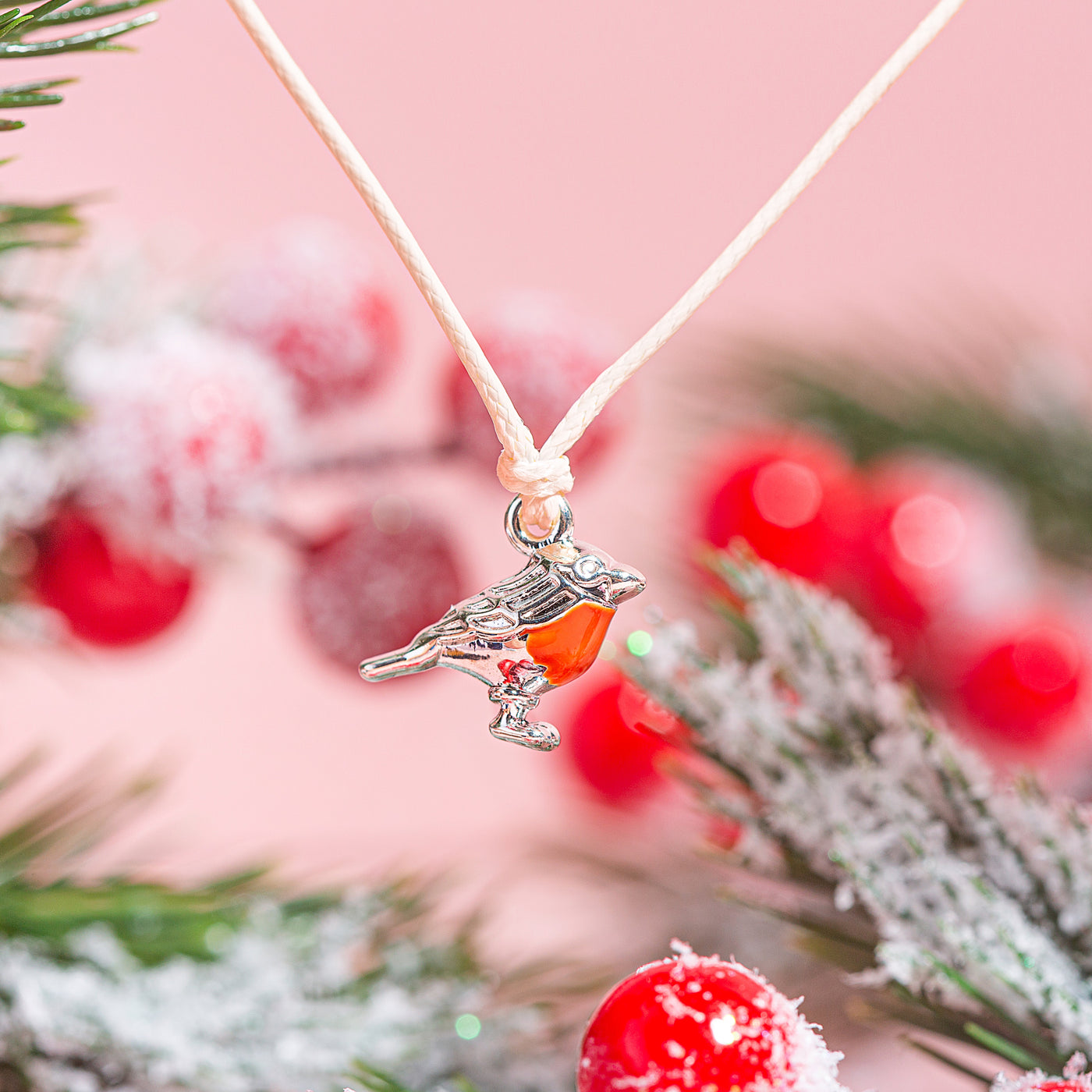 Necklace with a bird and berry pendant against a festive background with red berries and greenery.