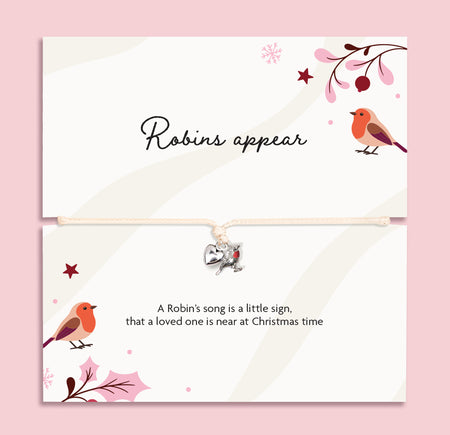A Christmas bracelet set featuring a top card with the script text 'Robins appear' to bring comfort in the festive season. The bracelet is adjustable with a small silver robin charm on a cream cord, set against a solid pink background.