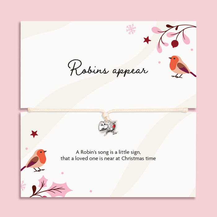 A Christmas bracelet set featuring a top card with the script text 'Robins appear' to bring comfort in the festive season. The bracelet is adjustable with a small silver robin charm on a cream cord, set against a solid pink background.
