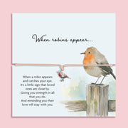 Adjustable sympathy bracelet with a silver robin charm on a blush cord, displayed on an illustrated keepsake card reading "When robins appear" with a comforting memorial poem