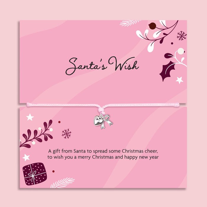 A pink Christmas-themed card or gift card set with decorative illustrations, the title 'Santa's Wish' on the top card, and a small silver bow charm tied across the bottom card. The design includes holly, pine branches, stars, and a gift box, all on a soft pink background. A perfect gift for Secret Santa.