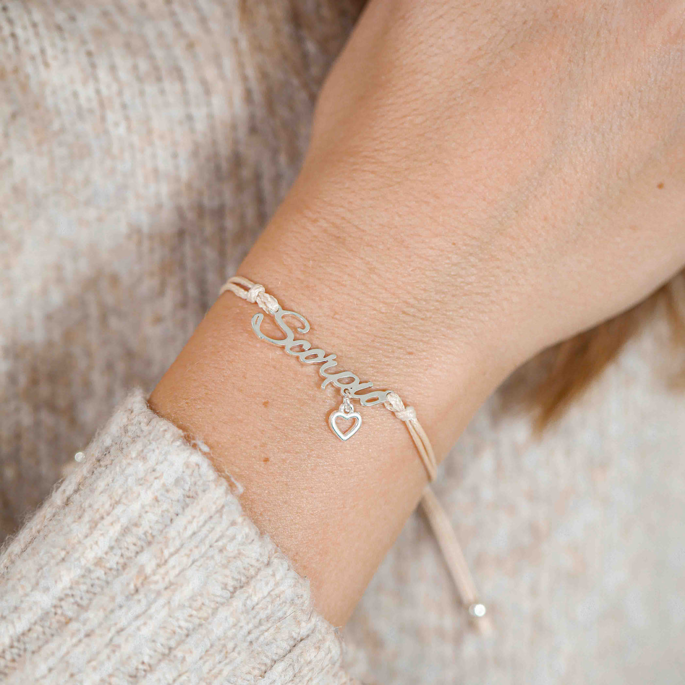 A woman wearing a dainty bracelet with the word “Scorpio” and a small heart charm, a thoughtful zodiac-inspired gift idea.
