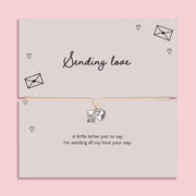 A pink background with 'sending love' poem card and heart envelope charm bracelet.