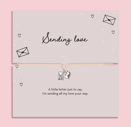 A pink background with 'sending love' poem card and heart envelope charm bracelet.