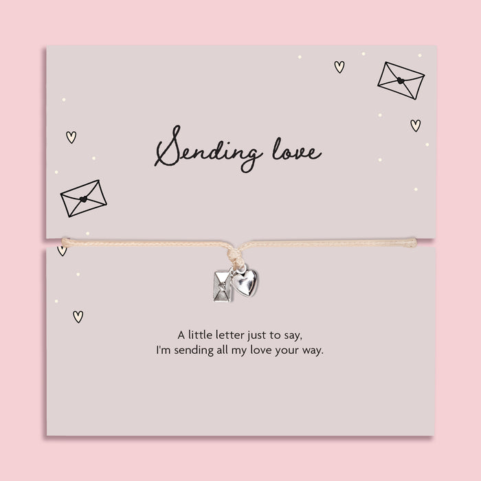 A pink background with 'sending love' poem card and heart envelope charm bracelet.