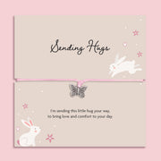 Pink string bracelet with a silver butterfly charm, displayed on a cream card with bunny illustrations and the message “Sending Hugs – I’m sending this little hug your way, to bring love and comfort to your day.