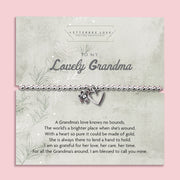 A silver beaded bracelet with a heart and flower charm displayed on a card reading "To my Lovely Grandma" from Letterbox Love, set against a soft pink background. The card includes a heartfelt poem, making it a perfect sentimental gift for a grandma.