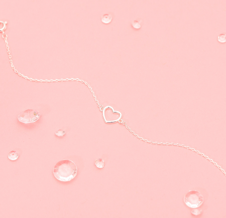 A pink background with small gem stones and a silver-plated hollow heart bracelet. An elegant gift for a bridesmaid to say thank you.