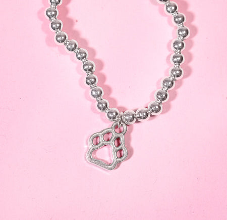 Silver beaded bracelet with a cute paw print charm on a pink background. A beautiful dog lover gift idea.