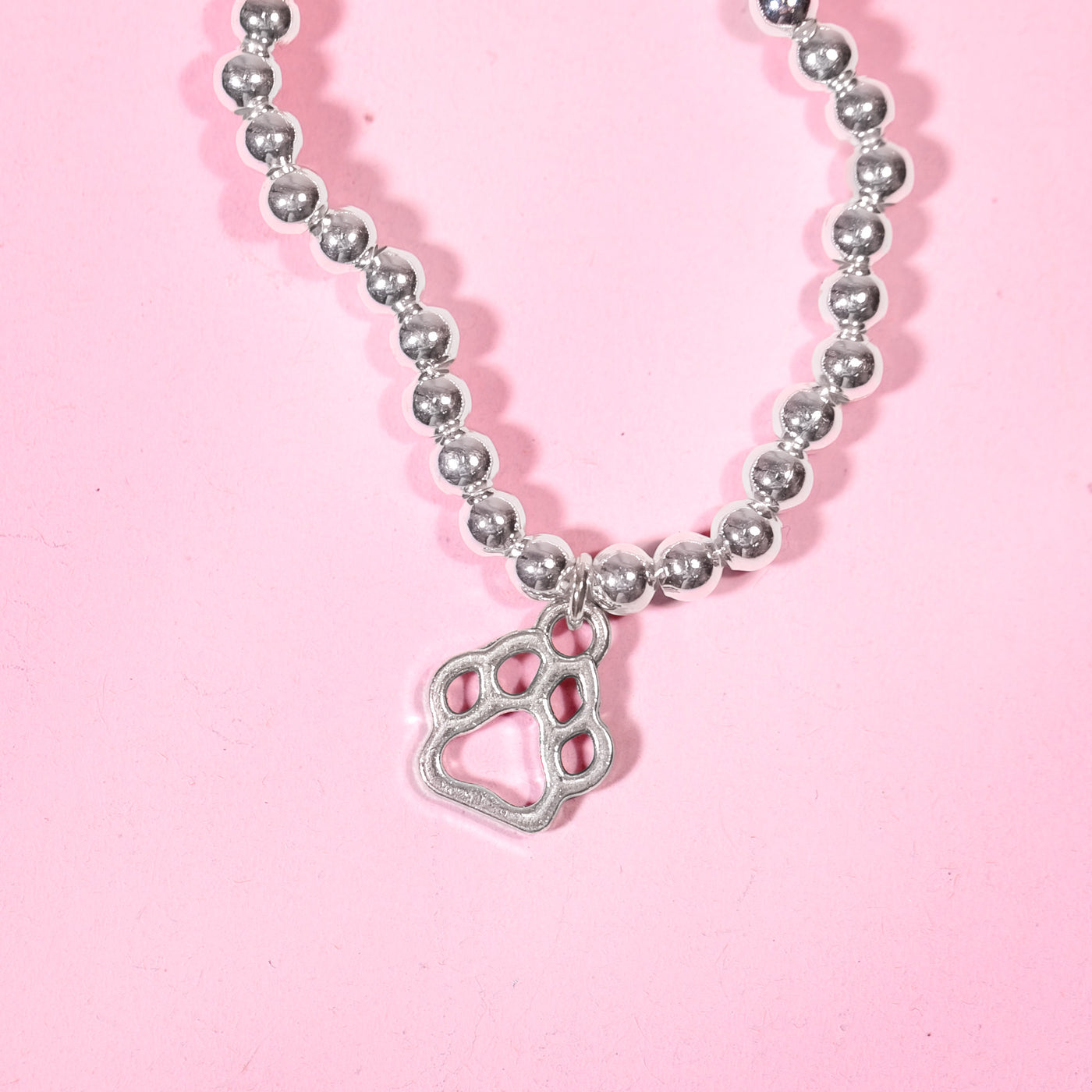 Silver beaded bracelet with a cute paw print charm on a pink background. A beautiful dog lover gift idea.