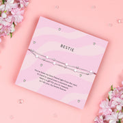 Silver-plated star bracelet on a pink wavy poem card with a meaningful sentiment for a friend. Making a perfect gift for a best friend on a pink background surrounded by gems and pink floral flowers.