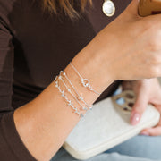 Person wearing multiple silver bracelets on wrist, holding a drink.