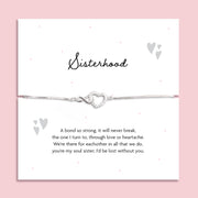 Silver-plated adjustable bracelet with an infinity heart charm, displayed on a white sentiment card titled "Sisterhood" with a heartfelt poem about soul sisters. Styled on a soft pink background with subtle heart and dot details.