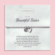 Silver beaded bracelet with heart and flower charms, displayed in a white gift box alongside a card titled "To My Beautiful Sister." The card features a heartfelt message celebrating the love and support of a cherished sister.