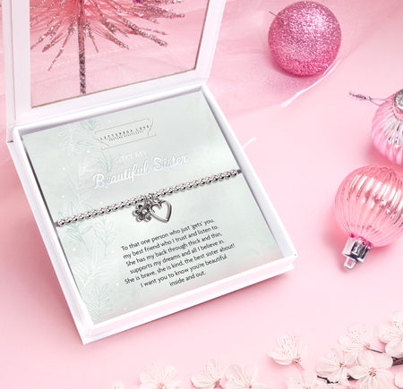 A delicate silver beaded bracelet with a heart and flower charm is beautifully displayed on a card that reads 